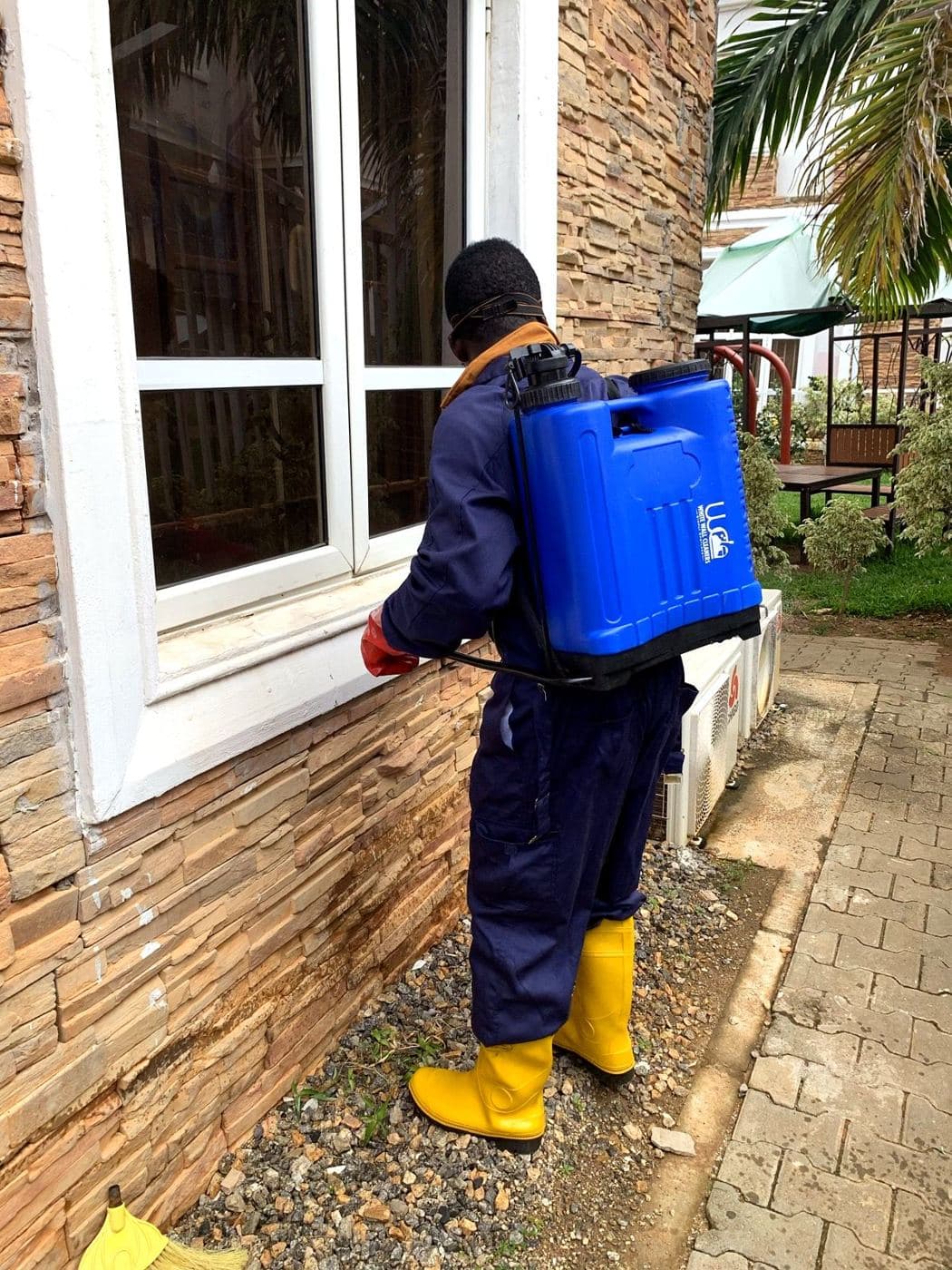 A White Wall crew member spraying along a wall with a knapsack sprayer
